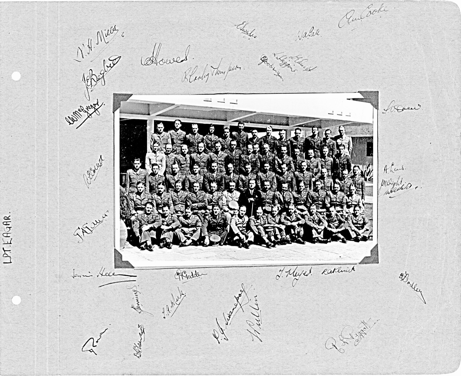 A group photograph of about seventy SAAF airmen in uniform outside a hotel, mounted on card covered in their signatures